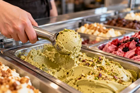 Pistazieneis wird mit dem Portionierer aus der Wanne genommen