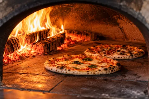 Zwei Pizzen im Holzofen neben dem Feuer